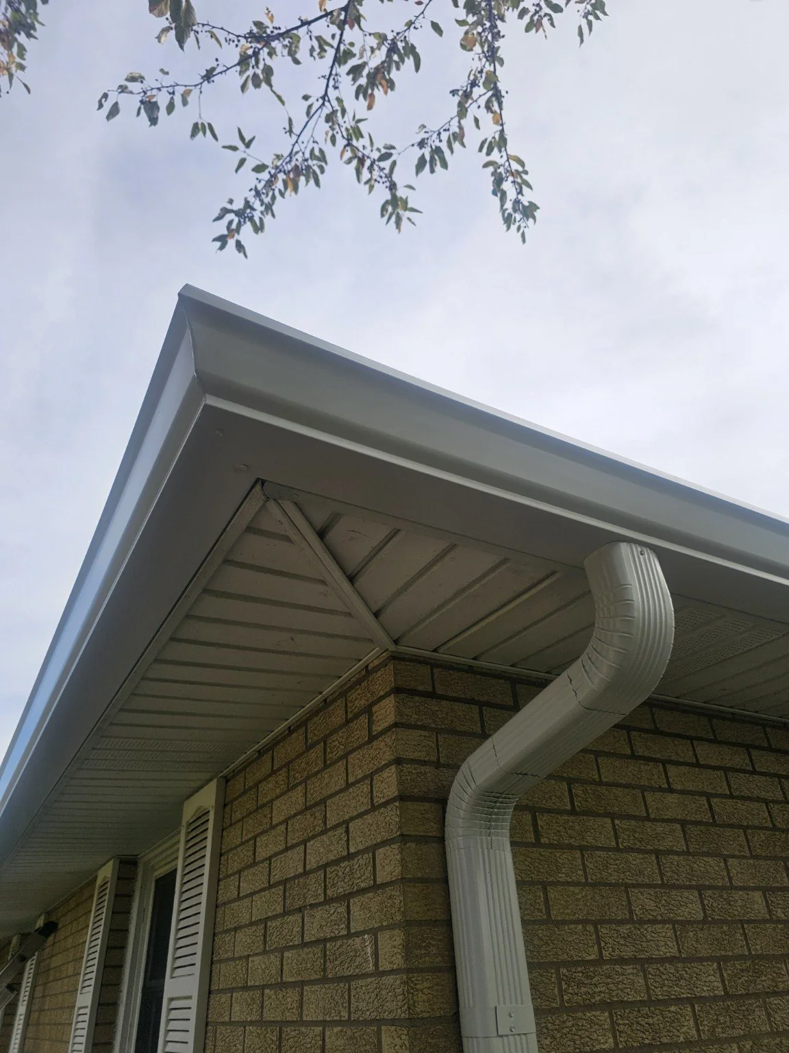 White seamless gutter and downspout installed on a brick home